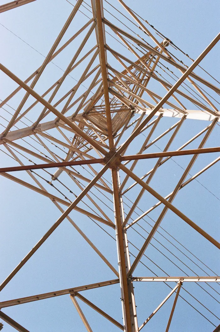 Looking straight up through a steel transmission tower against blue sky, shot on film